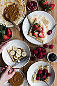 Top view of anonymous person taking bowl of tasty crepes with assorted toppings placed on lumber table during breakfast
