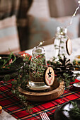 Christmas table setting with wreath and decorative wooden ornaments and red checkered tablecloth with yellow lights on the background