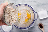 Top view of crop anonymous male pouring healthy almond flour into blender with eggs while cooking keto crepes in kitchen