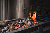 Heiße Flammen von brennendem Holz in einem schwarzen Metallkessel und glühende Holzkohle auf der Terrasse eines modernen Cafés bei der Vorbereitung zum Kochen
