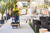 Female customer walking with shopping trolley in garden center and choosing pots for plants
