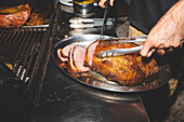 Anonymer männlicher Koch mit Zange, der gegrilltes Schweinefleisch auf einem Teller serviert, während er in der Nähe eines modernen Grills in einem Café steht