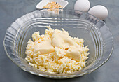 Glasschale mit Frischkäse und Mozzarella zum Backen von kohlenhydratarmen Bagels auf dem Tisch mit Eiern in einer hellen Küche