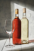 Composition of delicious semi sweet red and white wines in bottles placed near wineglass on plank table