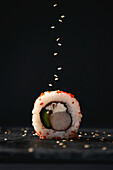 Appetizing tasty sushi roll with avocado and cheese placed on dark surface and served with sesame