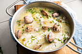 From above metal saucepan with delicious seafood soup with clams and hake placed on wooden board in kitchen