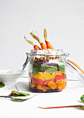 Salad with colorful ripe chopped bell peppers and bulgur topped with raw carrots served in jar on table against white background