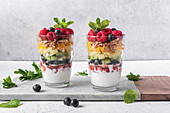 Appetitlicher Joghurt mit Schichten von frischen Früchten, serviert in Gläsern auf einem Tisch mit Minzblättern