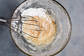 Glasschüssel mit Rohteig für gesunde Kaffee-Keto-Muffins mit Schneebesen auf dem Küchentisch, von oben gesehen