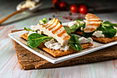 Tasty toasts with grilled chicken fillet and spinach leaves served on wooden cutting board near refreshing drink
