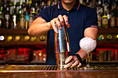 Hands of unrecognizable bartender holding a shaker for mixing a cocktail in the bar