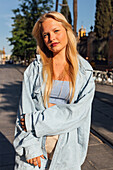 Charming female with blond hair and in trendy summer clothes standing in city and looking at camera