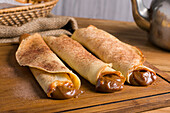Fresh rolled crepes filled with sweet dulce de leche filling served on wooden cutting board on table with kettle in kitchen