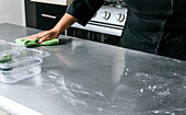 Crop unerkennbar weiblichen Koch in Uniform Abwischen von Edelstahl Küchentheke mit weichem Tuch im Restaurant