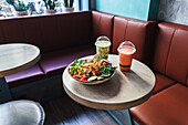 Leckerer Gemüsesalat mit Fleischstücken in einer Schüssel vor Einweggläsern mit erfrischenden Getränken auf einem Tisch in einem Innenraum