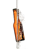 Brown glass bottle with metal lid behind splattering refreshing drink with bubbles in air