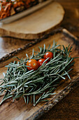 From above of whole ripe cherry tomatoes on fresh rosemary sprigs with pleasant scent on wooden plate