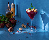 Glass goblet of tasty beetroot cream garnished with quail eggs and parsley placed near napkin with spoon and fresh ingredients against blue background