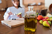 Young Asian woman halving ripe avocado over cutting board while cooking healthy salad following online recipe on laptop with black screen in kitchen at home