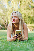 Charming female lying on grass in park and listening to music in headphones in summer