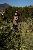 ethnic female farmer collecting ripe tomatoes in garden on sunny day in countryside