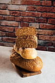 Pile of white and rye bread with cereals and appetizing crust on cutting board against brick wall in bakehouse