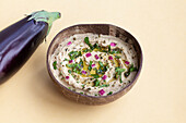 Fresh ripe aubergine placed on beige table with bowl of appetizing traditional Baba ghanoush dish