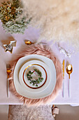 Von oben: weihnachtlich gedeckter Tisch mit Kranzdekoration und weißem und goldenem Geschirr auf flauschigem Tischset auf rosa Tischtuch