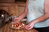 Unkenntlich gemachte ältere Frau mit reifen Feigenstücken in einer Schale auf einem Tisch in einem Haus mit unscharfem Hintergrund