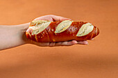 Unerkennbare Bäckerin demonstriert leckeres salziges Brezel-Baguette vor braunem Hintergrund in Backstube