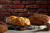 White and rye bread with cereals and appetizing crust on cutting board against brick wall in bakehouse