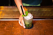 Die Hand eines unerkennbaren Barkeepers gibt Ihnen einen gut durchdachten Mojito-Cocktail in der Bar, nachdem er ihn zubereitet hat