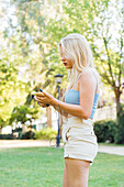 Side view of peaceful female in summer clothes listening to music in earphones while standing in park
