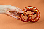 Unrecognizable female baker demonstrating delicious freshly baked pretzel with dark crust against brown background