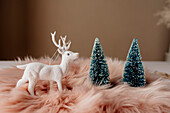 Von oben weihnachtlich gedeckter Tisch mit weißem Rentier auf flauschigem rosa Tischset neben blauem Tannenbaum