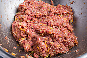 From above of raw minced meat with carrot and onion mixed in steel bowl