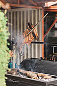Crop faceless person standing with delicious pork ribs in hand over hot grill with firewood on terrace of light cafe