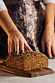 Anonyme Bäckerin hält Brot mit Sonnenblumenkernen auf einem Tisch in einer Backstube