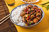 Von oben Kompositionsschüssel mit Kung-Pao-Hühnchen mit weißem Reis, Erdnuss, roter Chilischote, grünen Zwiebeln und Stäbchen