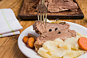 Leckeres hausgemachtes Corned Meat mit Kohlstücken und Karotten auf einem Teller auf einem Holztisch serviert