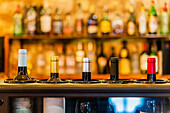 Glasflaschen mit Rotwein auf einem Bartresen in einem Restaurant vor einem unscharfen Regal mit Flaschen mit alkoholischen Getränken
