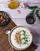 From above of bowl with traditional Bulgarian cold summer soup tarator with yogurt placed near glass of water and plate with nuts