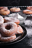 Sweet fried doughnuts served on plate near metal cooling rack a on black messy table with powdered sugar