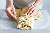 Crop unrecognizable female chef preparing delicious apple pastry with soft braided dough and fruit slices in house