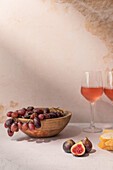 Glasses of red drink placed on table with bowl of grapes and figs near baguette slices