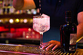 Junge asiatische Barkeeperin gießt Tonic Water ins Glas, um einen Gin-Tonic-Cocktail in der Bar zuzubereiten