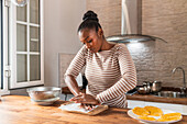Young African American female crushing fresh plantain on cutting board while preparing patacones at home