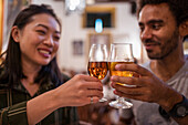 Soft focus of multiracial couple clinking glasses of alcohol drinks while having dinner together in modern restaurant during festive event