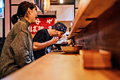 Seitenansicht einer Frau und eines Mannes, die sich beim Essen asiatischer Speisen an einem Holztresen in einem modernen Café unterhalten