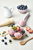 Yummy berry ice cream scoops on crispy waffle bowl decorated with fresh ripe strawberries blueberries pistachio and mint leaves against white background